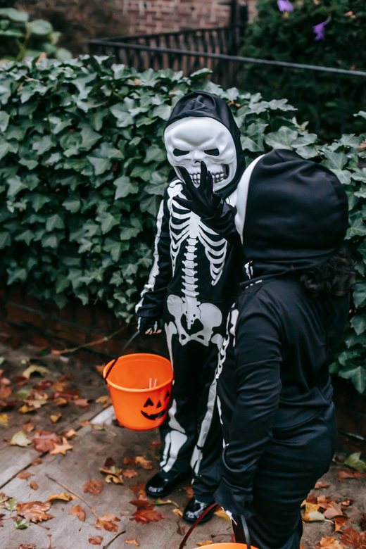 A child in a skeleton costume holding a Halloween candy bucket