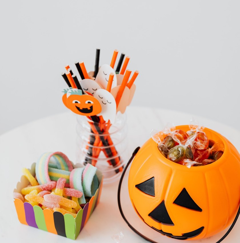 Halloween candy, treat cups, and a pumpkin bucket arranged on a table